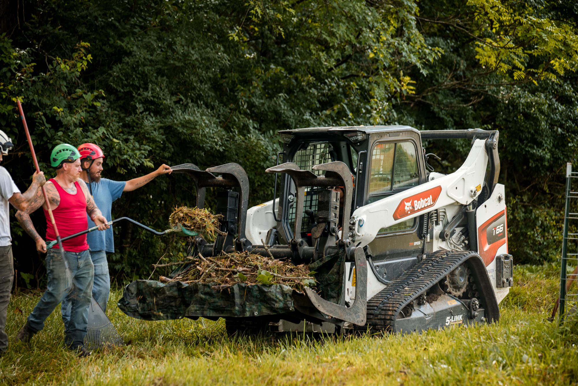 Crew members loading cut limbs into a grapple attachment in an open field
